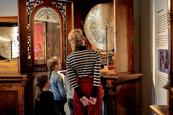 Eine Erwachsene und zwei Kinder betrachten einen Musikautomaten