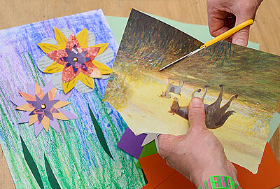 Hände schneiden und gestalten bunte Papierblumen neben einem Ausdruck eines Gemäldes. Der kreative Workshop verbindet Kunstbetrachtung, florale Motive und Kulturvermittlung im Programm Bloom up! des Badischen Landesmuseums.
