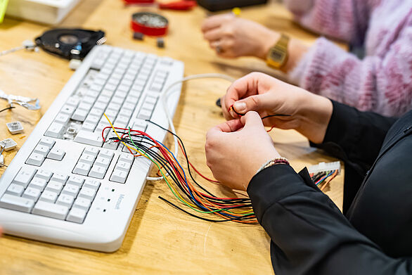 Hände flechten mit alten Elektrokabeln vor einer Tastatur