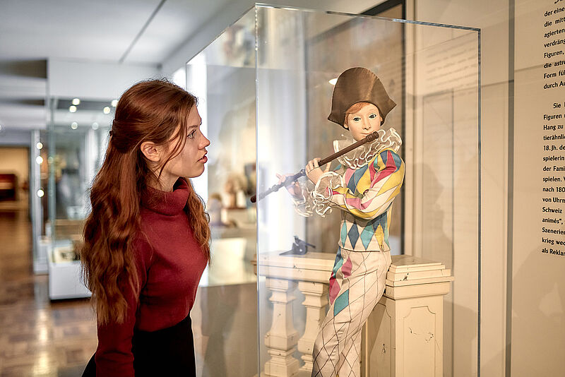 Besucherin, die sich eine Figur eines Flötenspielers in einer Vitrine ansieht